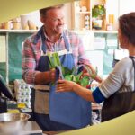 A stack of 100 navy blue reusable non-woven tote bags with handles, neatly folded and ready for use.