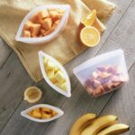 Four clear Stasher reusable silicone bags, including snack, sandwich, 2-cup, and 4-cup sizes, neatly arranged.